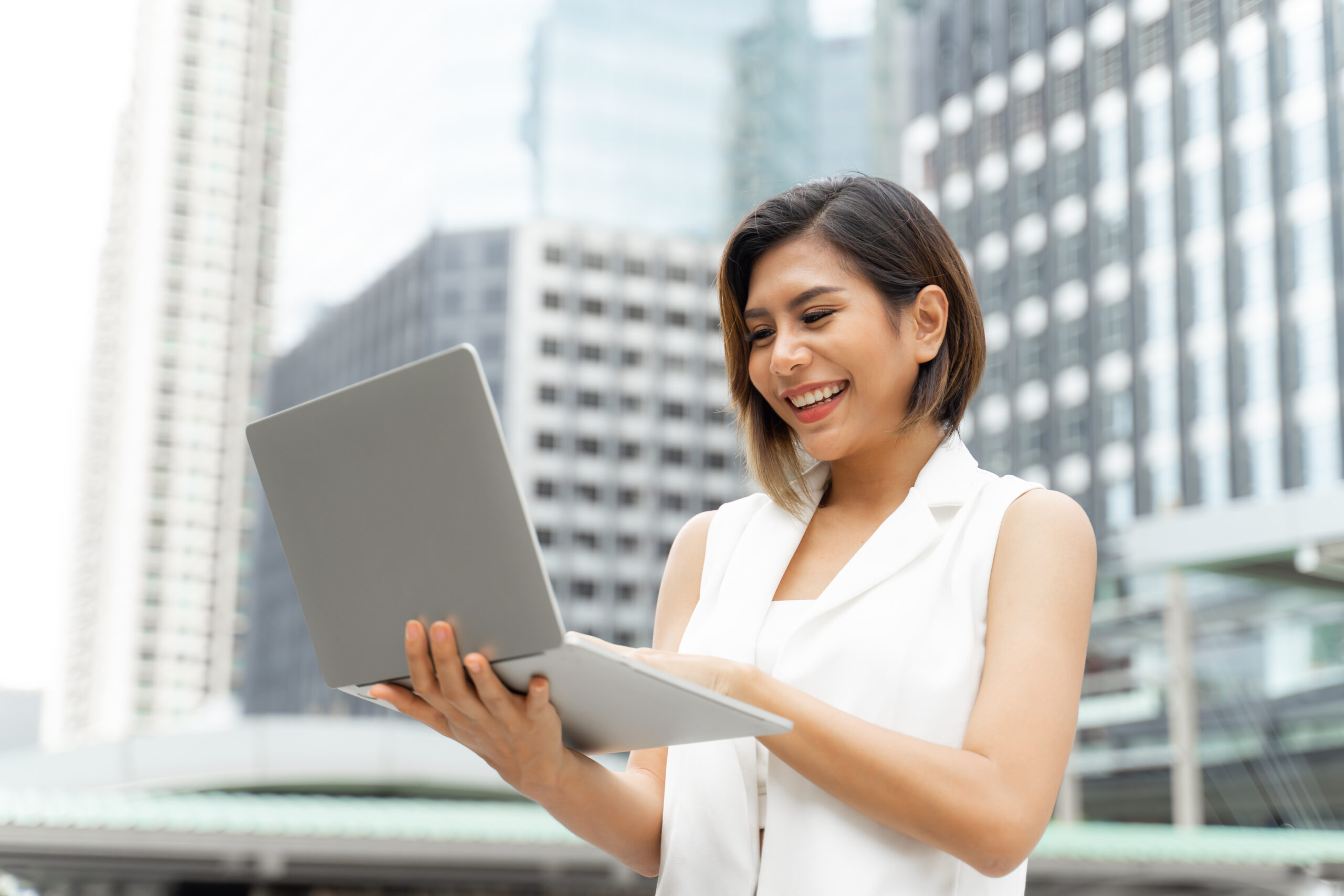 A beautiful young woman, dressed in professional business attire, smiling as she works on a domain transfer using her laptop.
